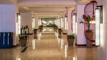 A hotel lobby with a long corridor, potted plants, and modern lighting fixtures.