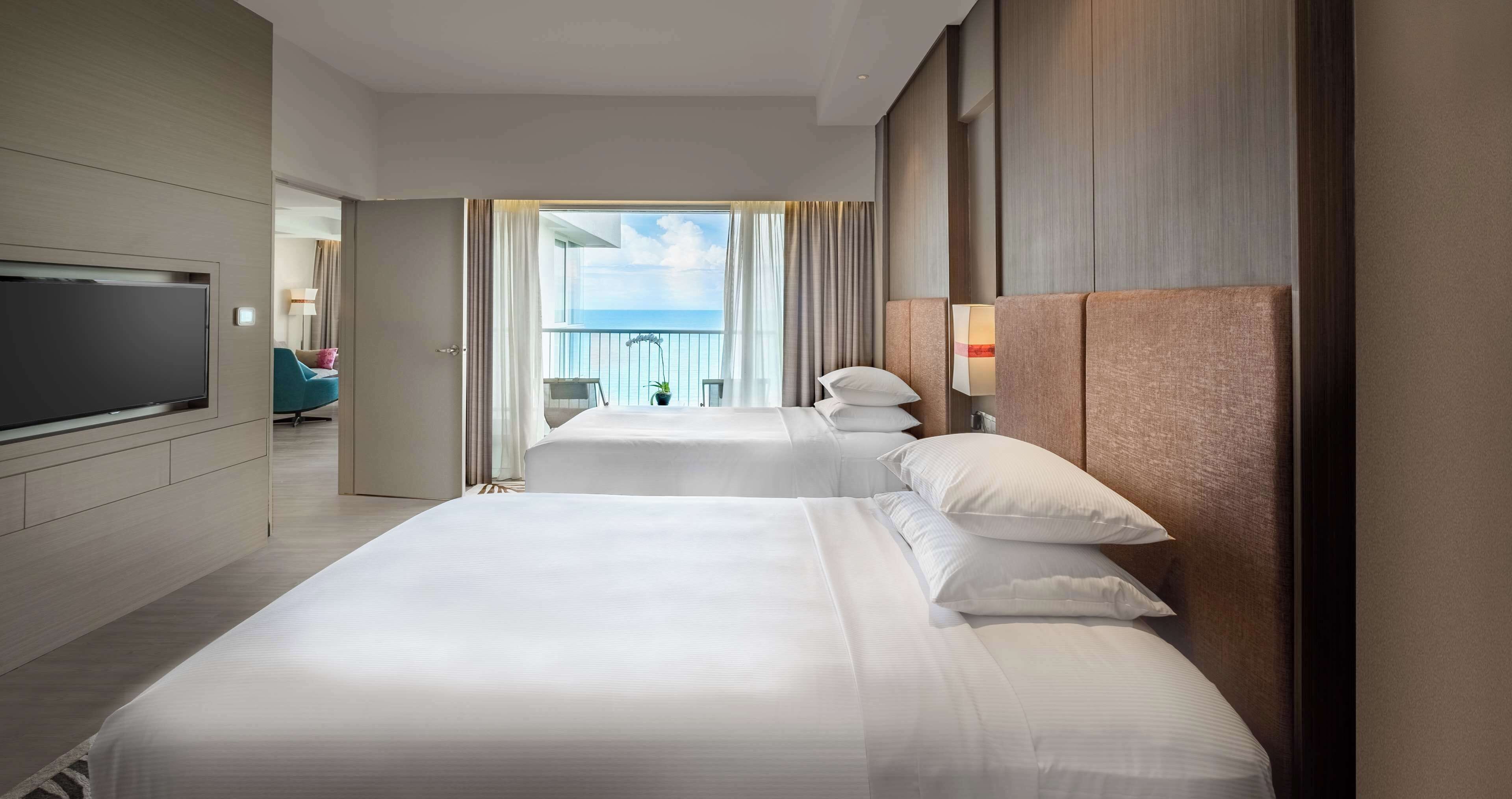 Een hotelkamer met een groot bed, een televisie en een balkon met uitzicht op zee.