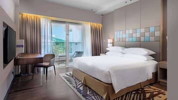 A hotel room with a bed, a desk, a chair, a TV, and a balcony with curtains.