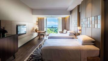 A hotel room with two beds, a desk, a TV, and a balcony with a view.