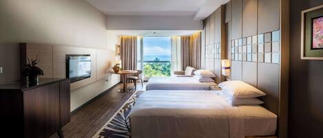 A hotel room with two beds, a desk, a TV, and a balcony with a view.