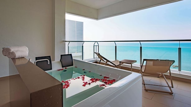 Ein moderner Balkon mit einem gläsernen Whirlpool, einem Sessel und Blick aufs Meer.