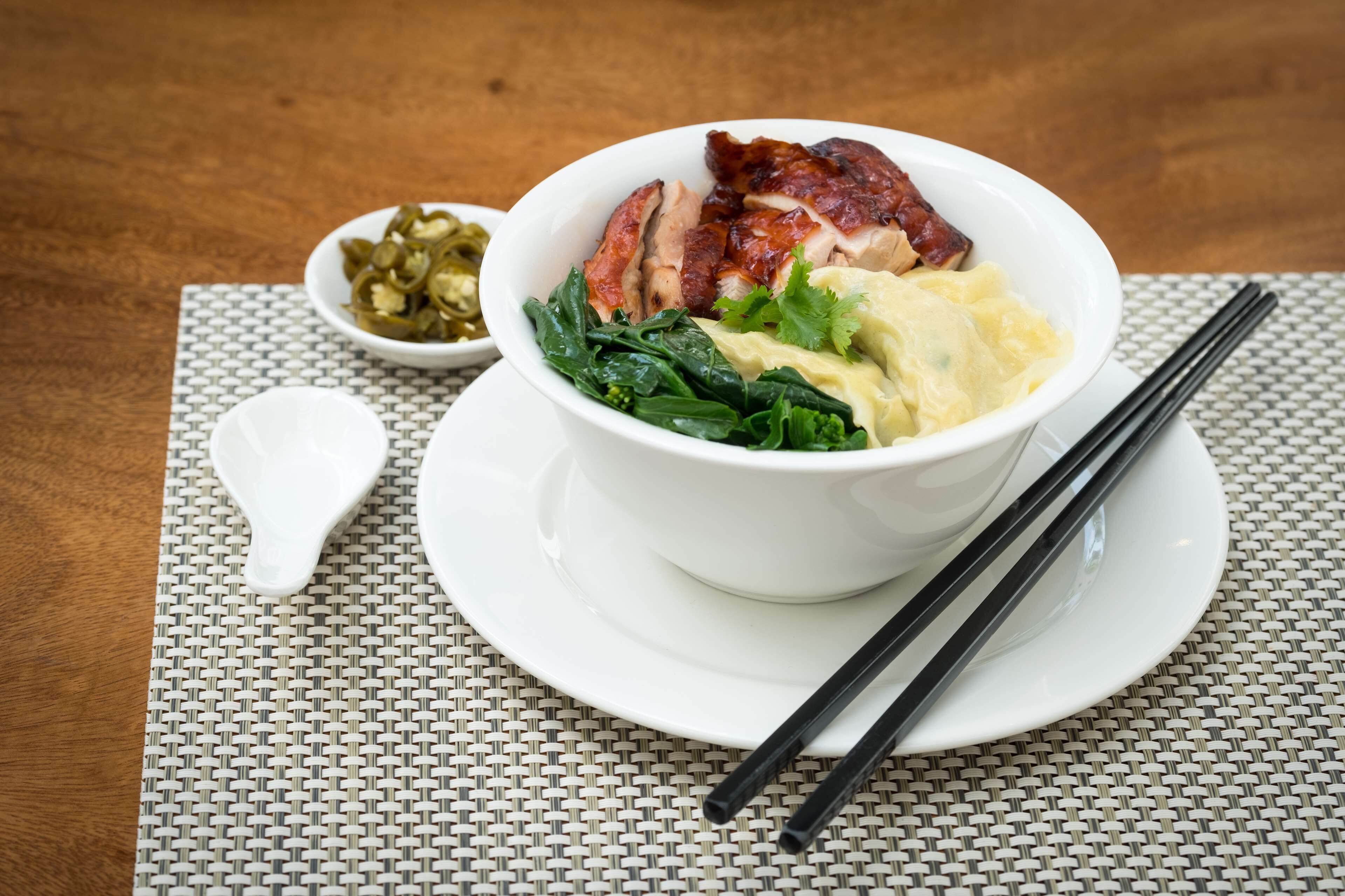 A bowl of food with chopsticks and a spoon on a woven placemat.