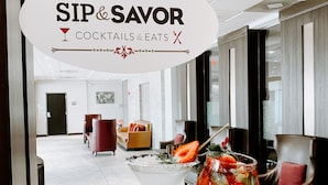 Un hall d’hôtel comprenant un comptoir d’accueil, un espace salon et un panneau indiquant : « DÉGUSTEZ DES COCKTAILS ET DES PETITS PLATS ».