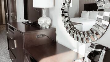 Habitación de hotel con minibar, espejo con diseño de mosaico y cama con ropa blanca.