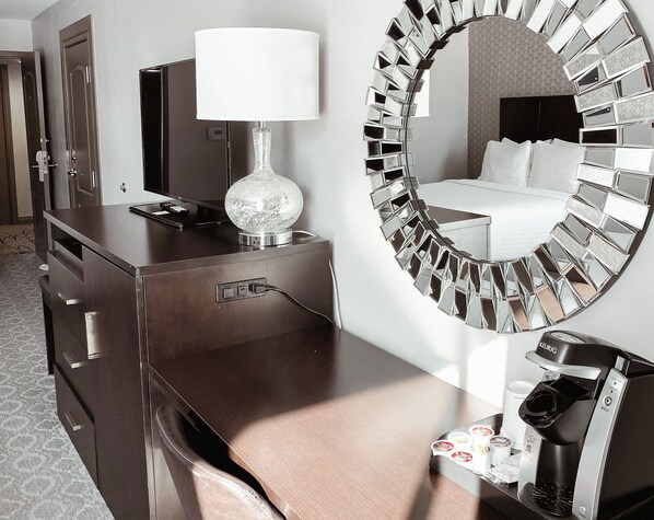 A hotel room with a minibar, a mirror with a mosaic design, and a bed with white bedding.