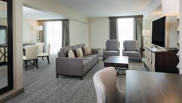 Una habitación de hotel con un sofá gris, dos sillones, una mesa de centro, un televisor y un escritorio con una lámpara.