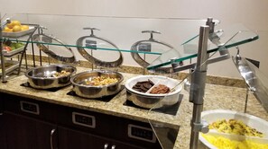 A buffet setup with various food items in metal bowls, a glass display case, and a stainless steel counter.