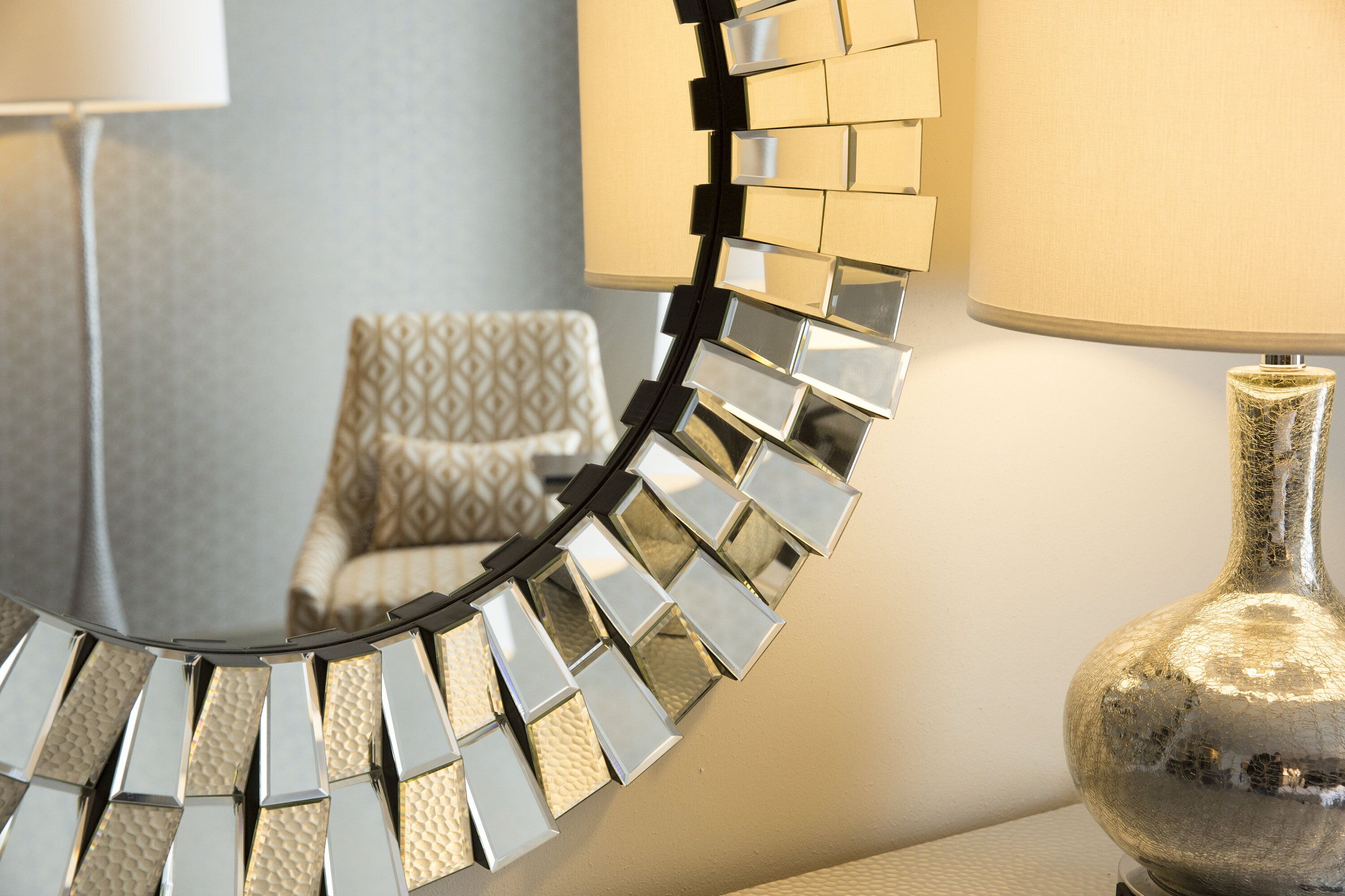 Een spiegel met een geometrisch frame, een lamp met een structuurvaste voet, en een gestreept stoel op de achtergrond.