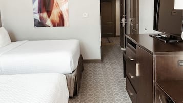 Ett hotellrum med två sängar, en tv, en byrå och en tavla på väggen.