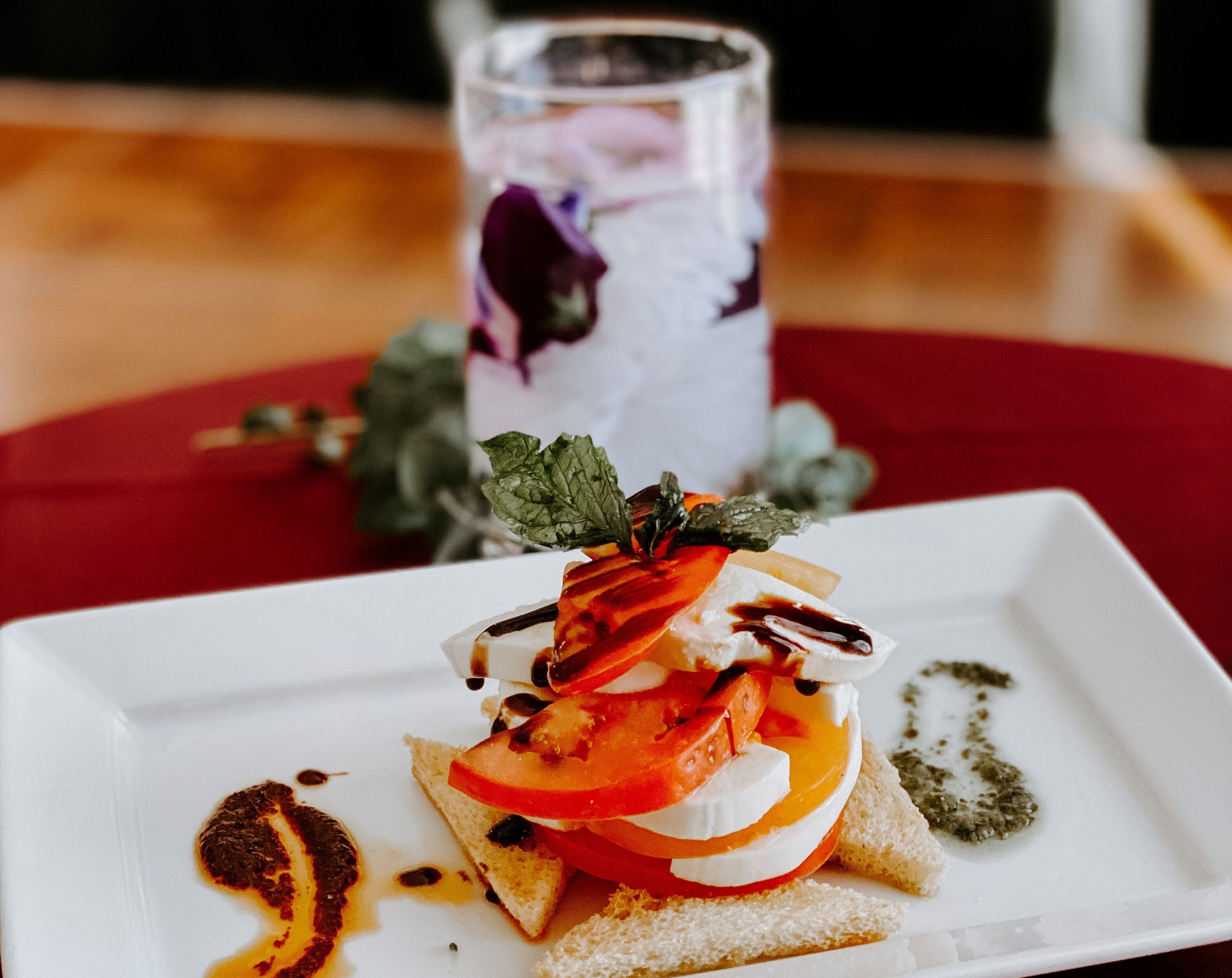 Une assiette carrée blanche sur laquelle est servie une salade, le tout posé sur une nappe rouge.