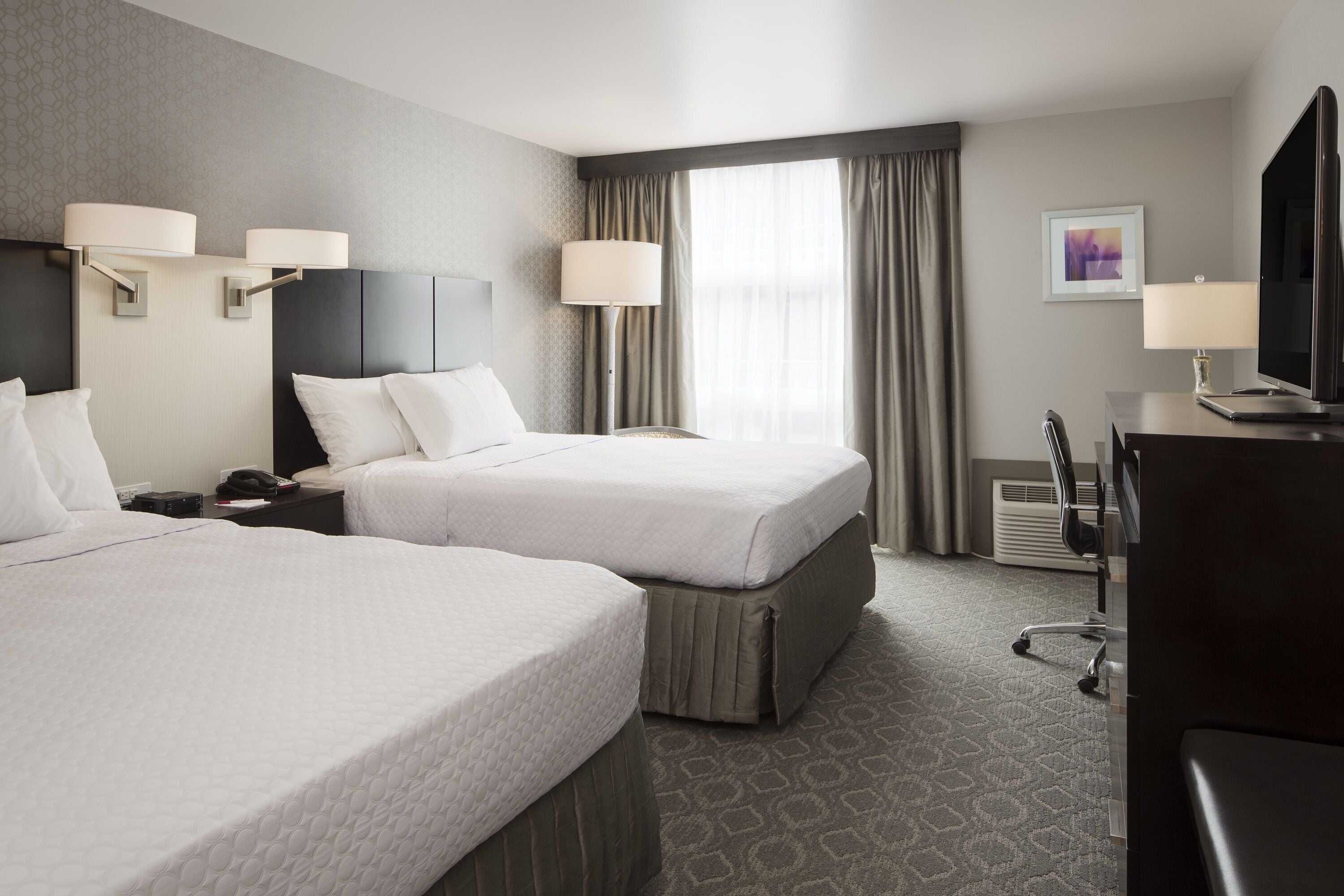 A hotel room with two beds, a desk with a computer, a TV, and a chair.