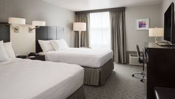 A hotel room with two beds, a desk with a computer, a TV, and a chair.