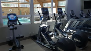 Une salle de sport équipée de tapis de course, de vélos elliptiques et offrant une vue sur une piscine extérieure.