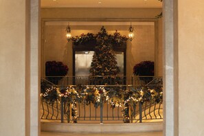 Un sapin de Noël décoré de guirlandes lumineuses et d’ornements, une rambarde de balcon et un luminaire fixé au mur.