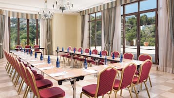 A conference room with a long table, red chairs, and large windows with curtains.