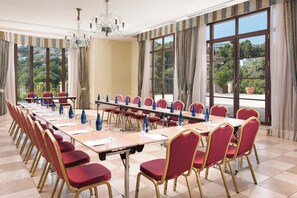 Une salle de conférence avec une longue table, des chaises rouges et de grandes fenêtres dotées de rideaux.