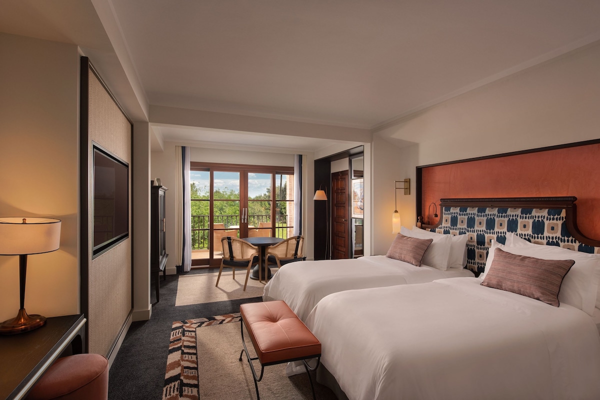 Une chambre d’hôtel avec deux lits, un bureau, une chaise, une petite table et un balcon avec vue.