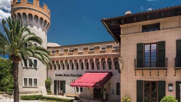 Un edificio histórico con una torre, un toldo rojo y una palmera.