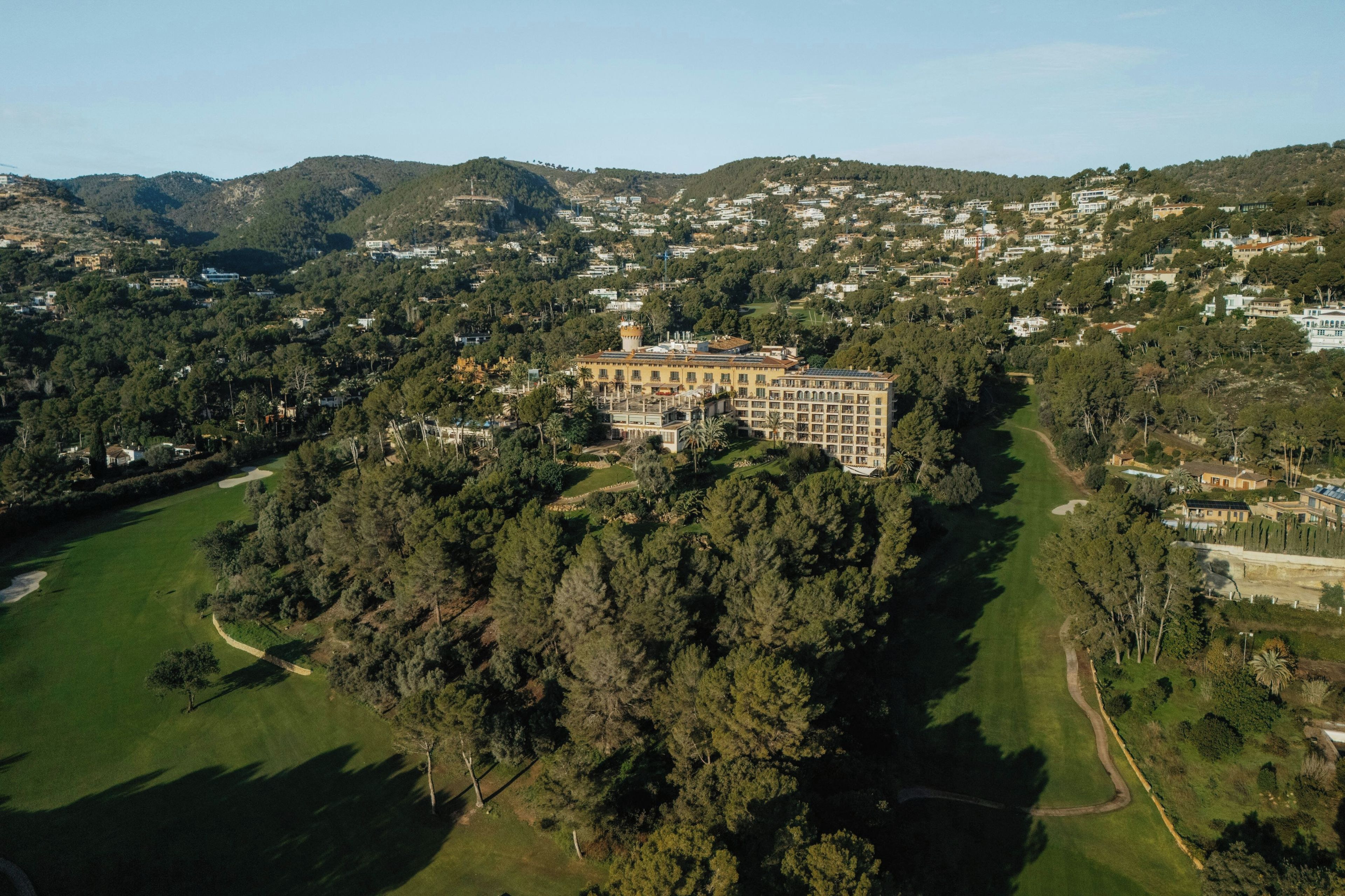 An aerial view of a large building surrounded by dense forest and a golf course.