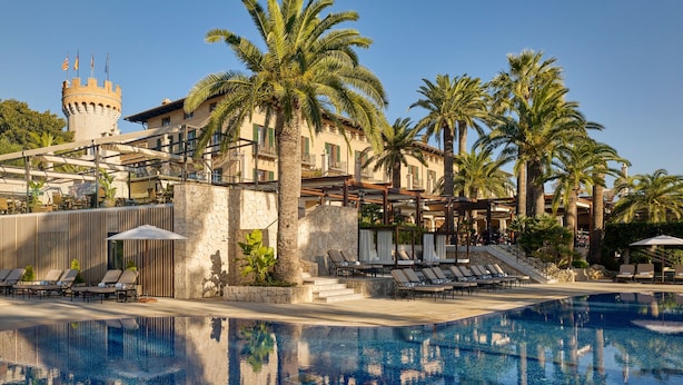 Ein Resort mit Schwimmbad, Palmen und einem schlossartigen Gebäude im Hintergrund.