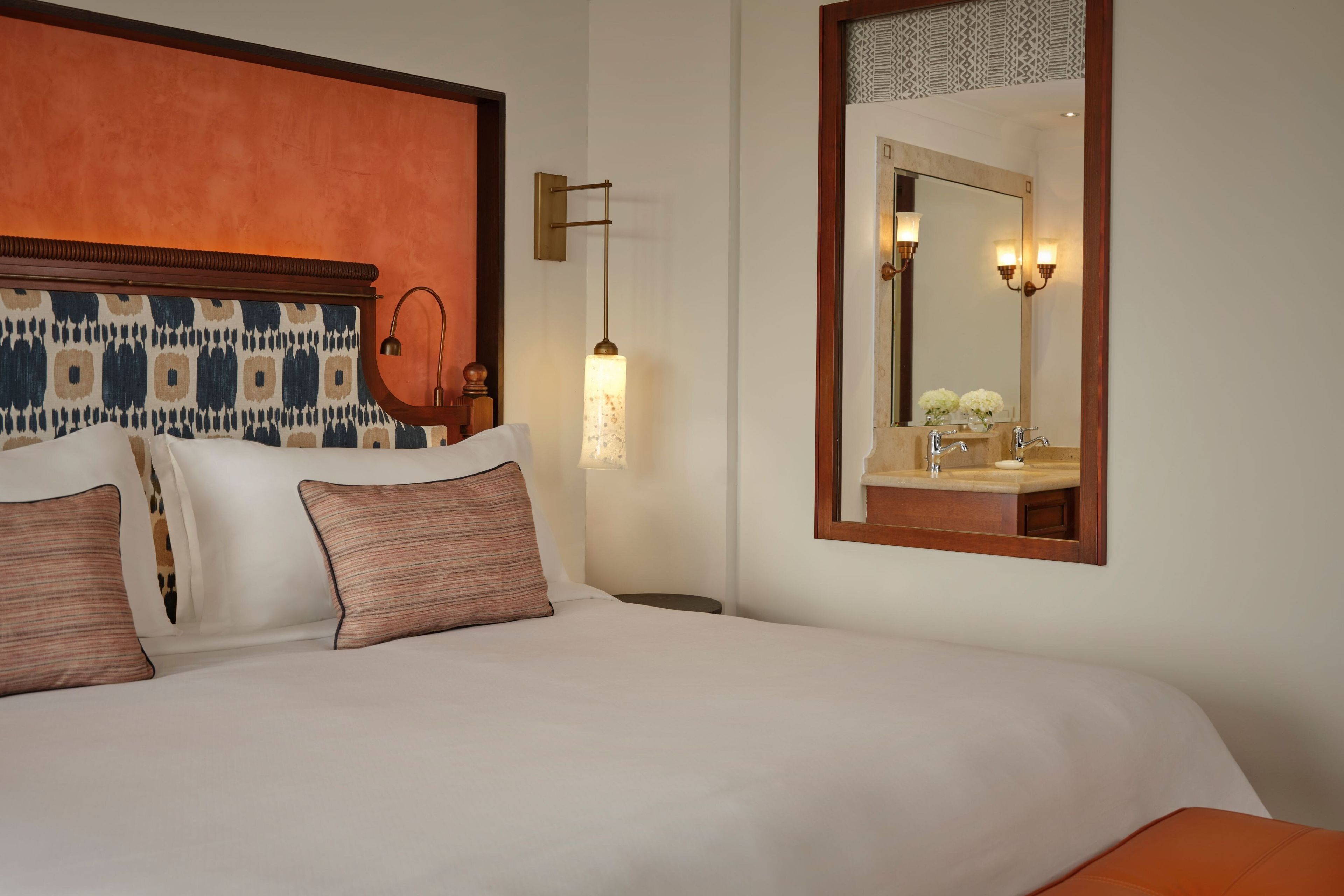 Une chambre d’hôtel comprenant un lit, une table de chevet, une lampe, un miroir et un luminaire fixé au mur.