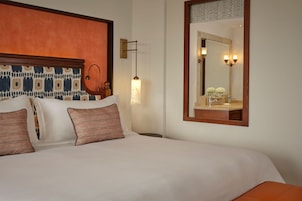 Habitación de hotel con cama, mesita de noche, lámpara, espejo y aplique de pared.