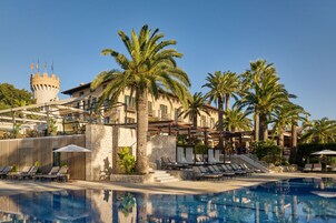 Un resort con piscina, palmeras y un edificio con aspecto de castillo al fondo.