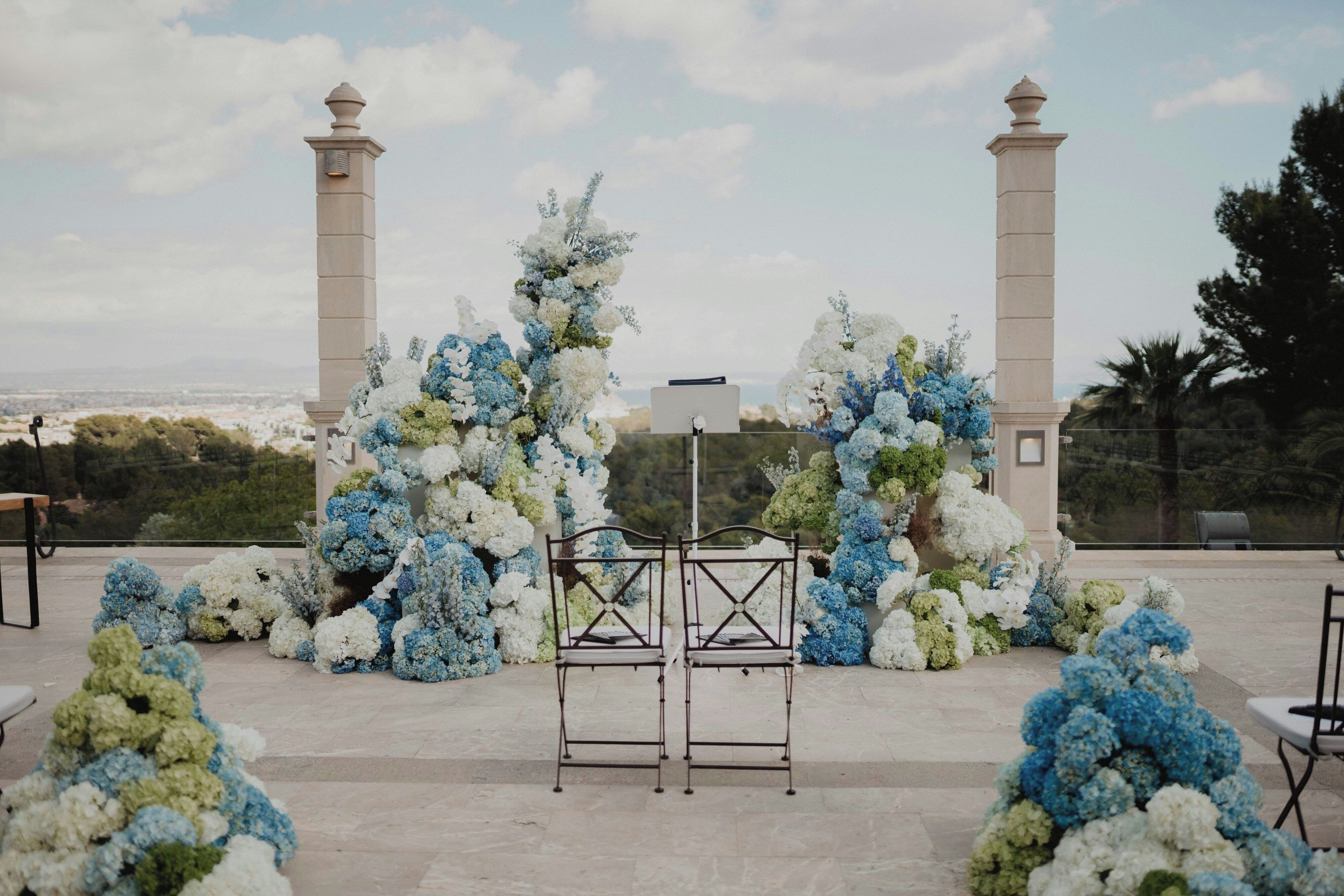 Decoración para boda al aire libre con un arco floral blanco y azul, dos columnas altas y un atril de metal.