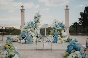 Allestimento per matrimonio all'aperto con arco floreale bianco e blu, due colonne alte e un leggio in metallo.