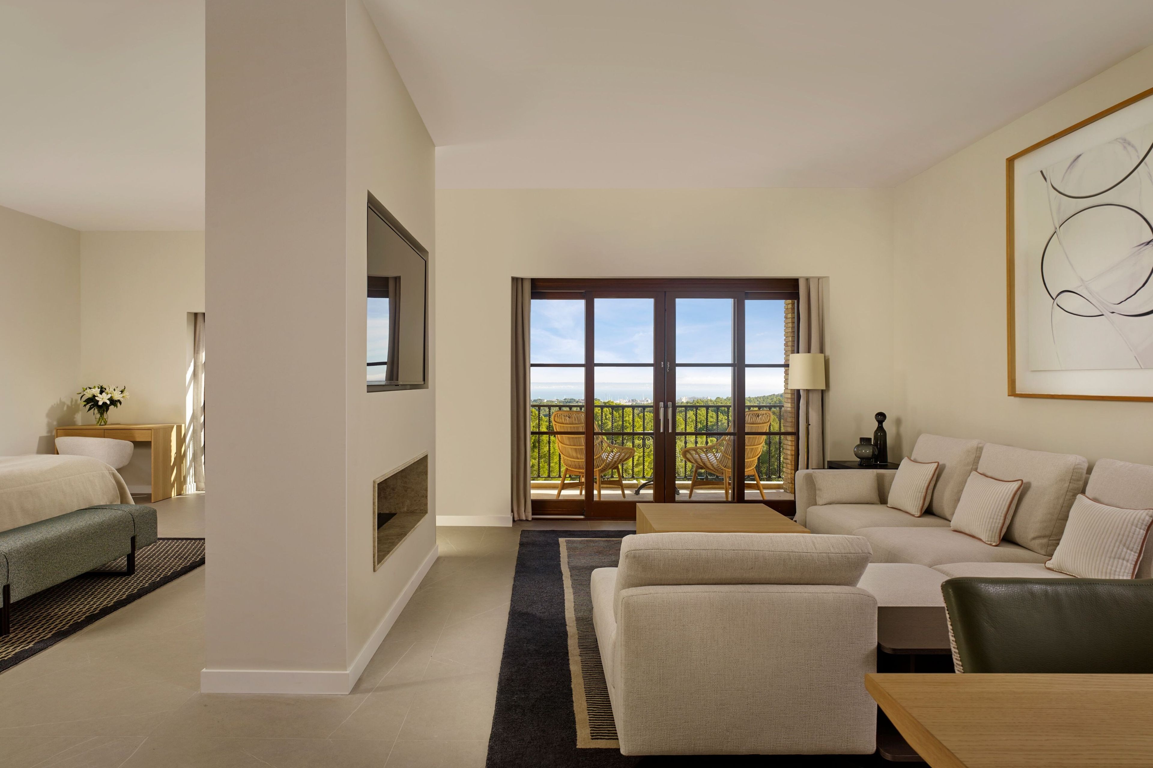 A modern hotel room with a balcony, a sofa, a bed, and a dining area.