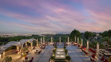 A rooftop terrace with red chairs and tables, a central water feature, and a view of the cityscape.
