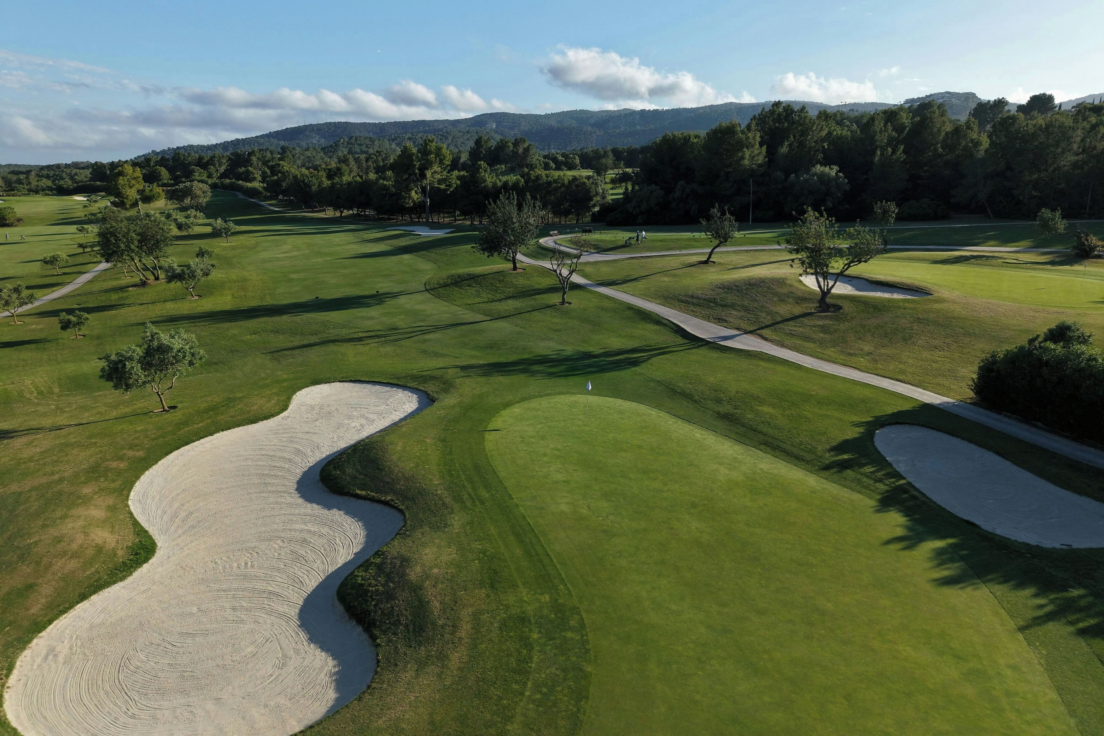 A golf course with sand bunkers, pathways, and trees.