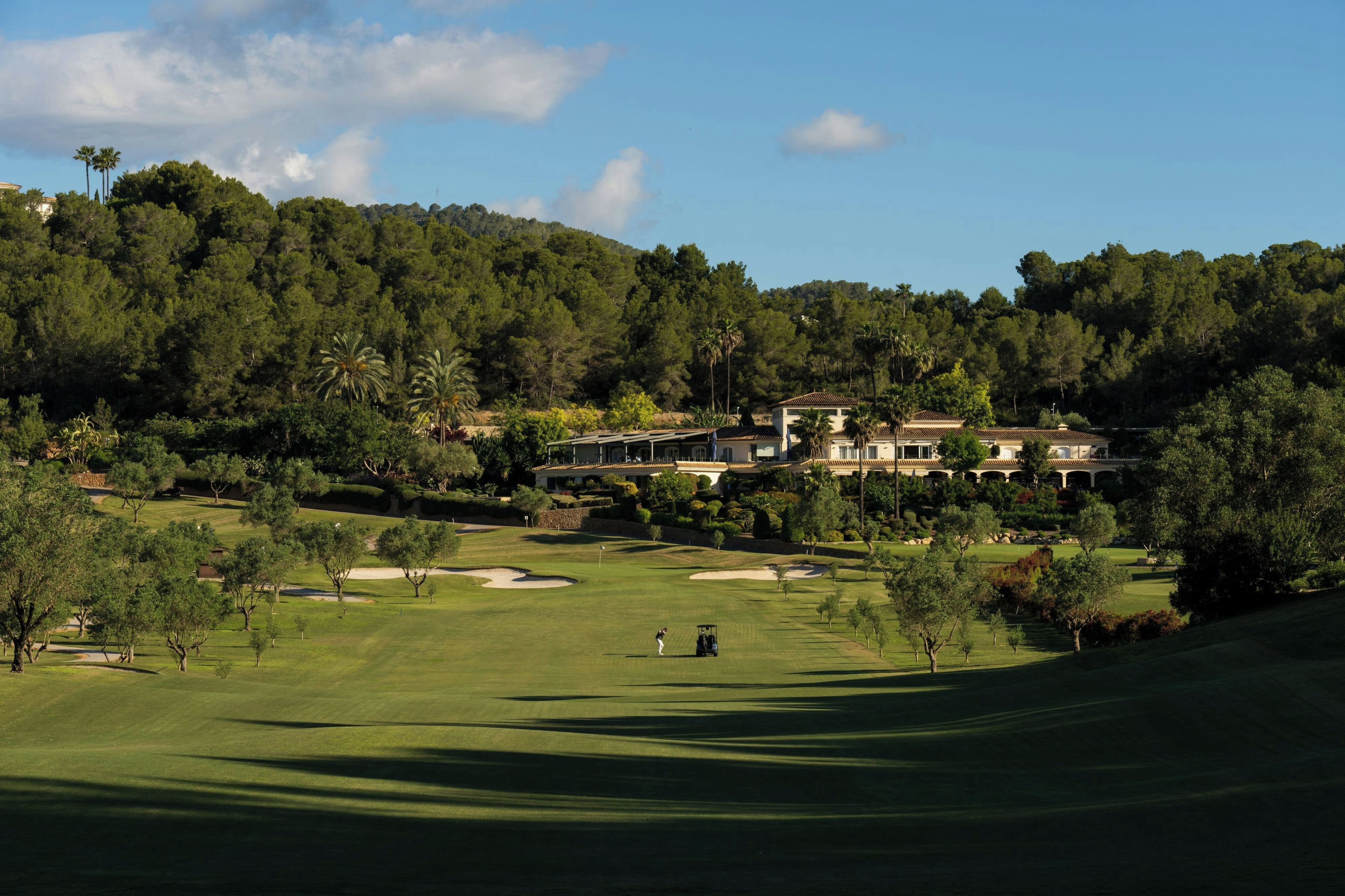 Un campo de golf con un club de campo y edificios residenciales al fondo.