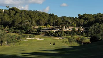 Un campo de golf con un club de campo y edificios residenciales al fondo.
