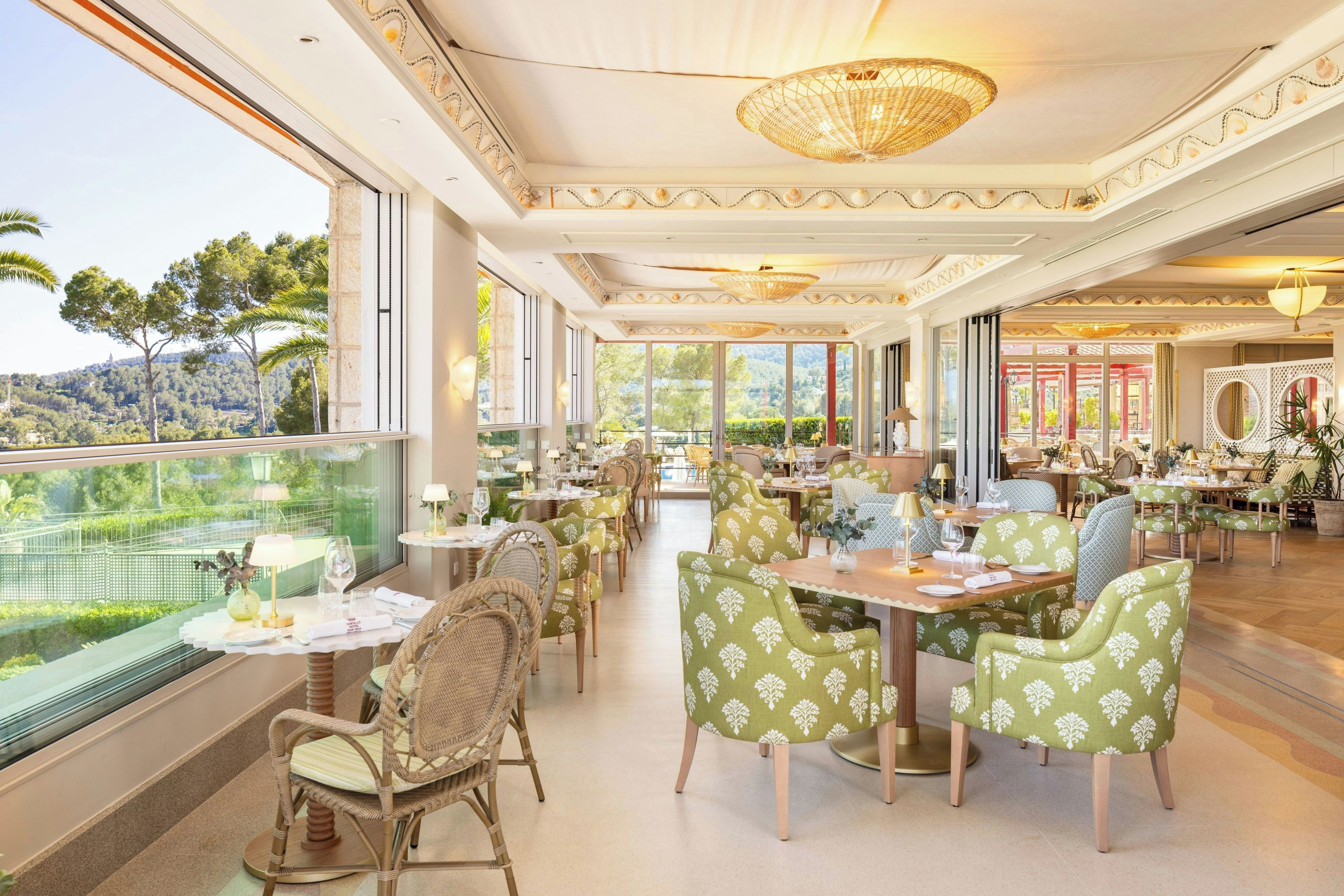 A restaurant with a view of a mountainous landscape, featuring a high ceiling with decorative moldings and a central chandelier.