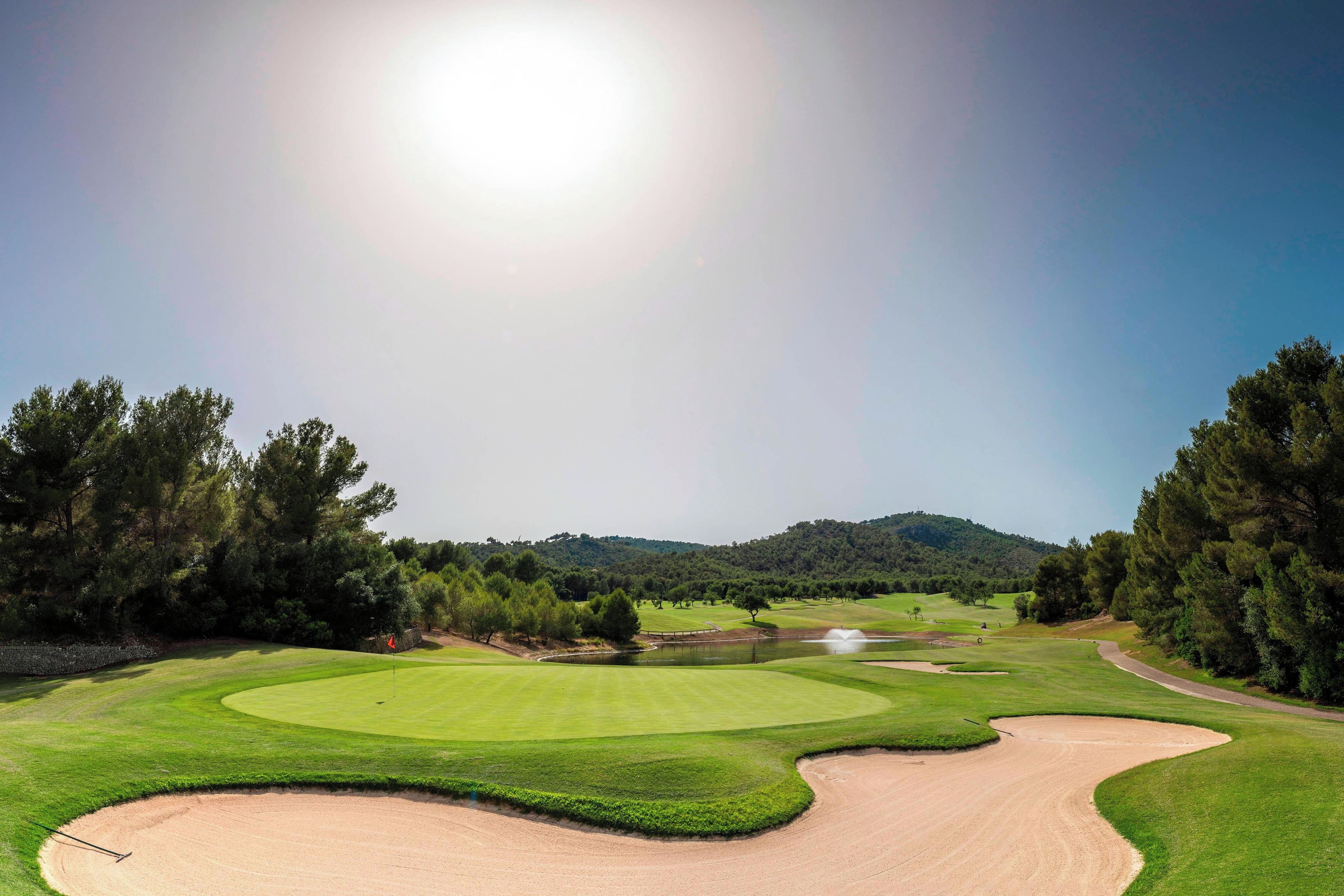Campo de golf con un bunker de arena, peligros de agua y cielo despejado.