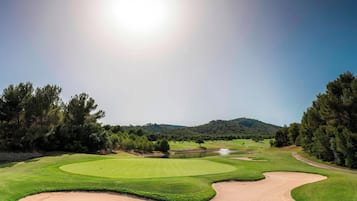 Campo de golf con un bunker de arena, peligros de agua y cielo despejado.