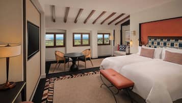 A hotel room with a large bed, a desk, a chair, a small table, and a view of the sea through the windows.