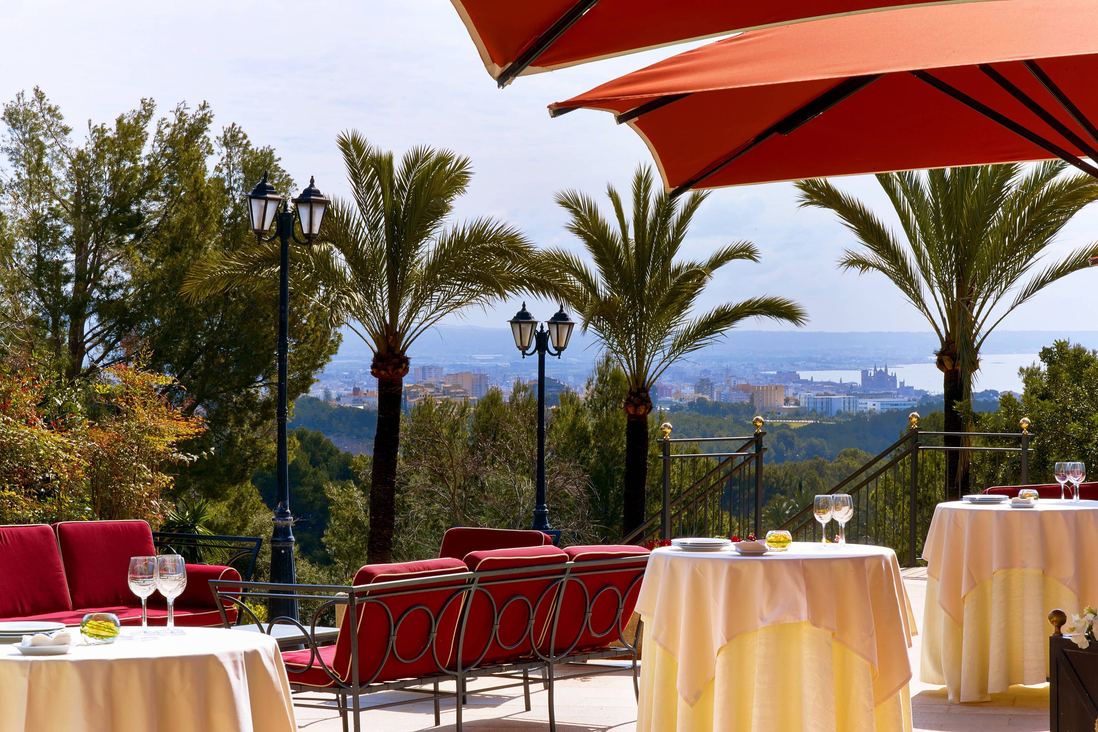 Un espace de restauration en plein air, avec des chaises et des tables rouges, offrant une vue panoramique sur la ville et les montagnes.