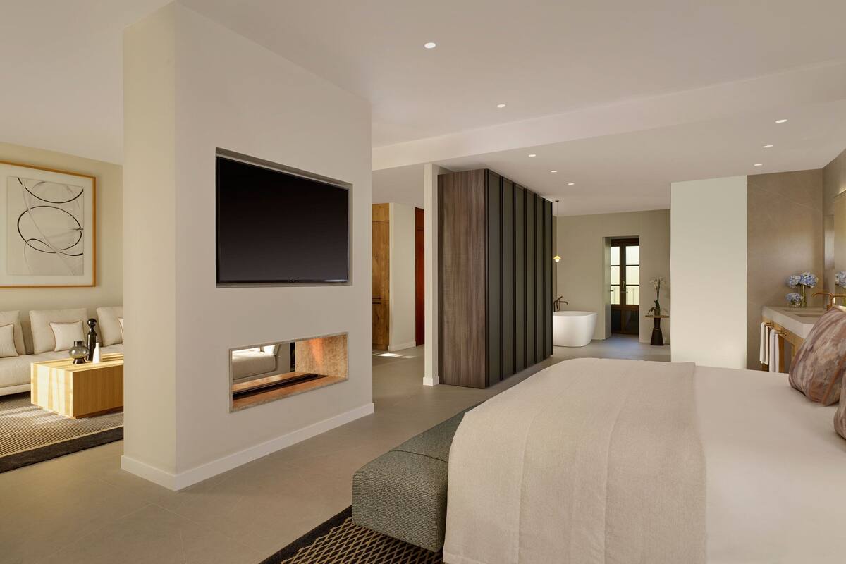 Une chambre d’hôtel moderne dotée d’un grand lit, d’un téléviseur à écran plat fixé au mur, d’un petit coin salon avec une table basse et d’une salle de bain visible à travers une porte ouverte.