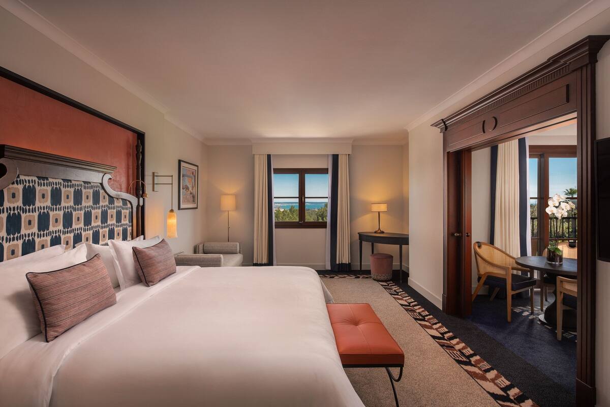 Une chambre d’hôtel avec un grand lit, un bureau, une chaise et une vue sur l’extérieur.