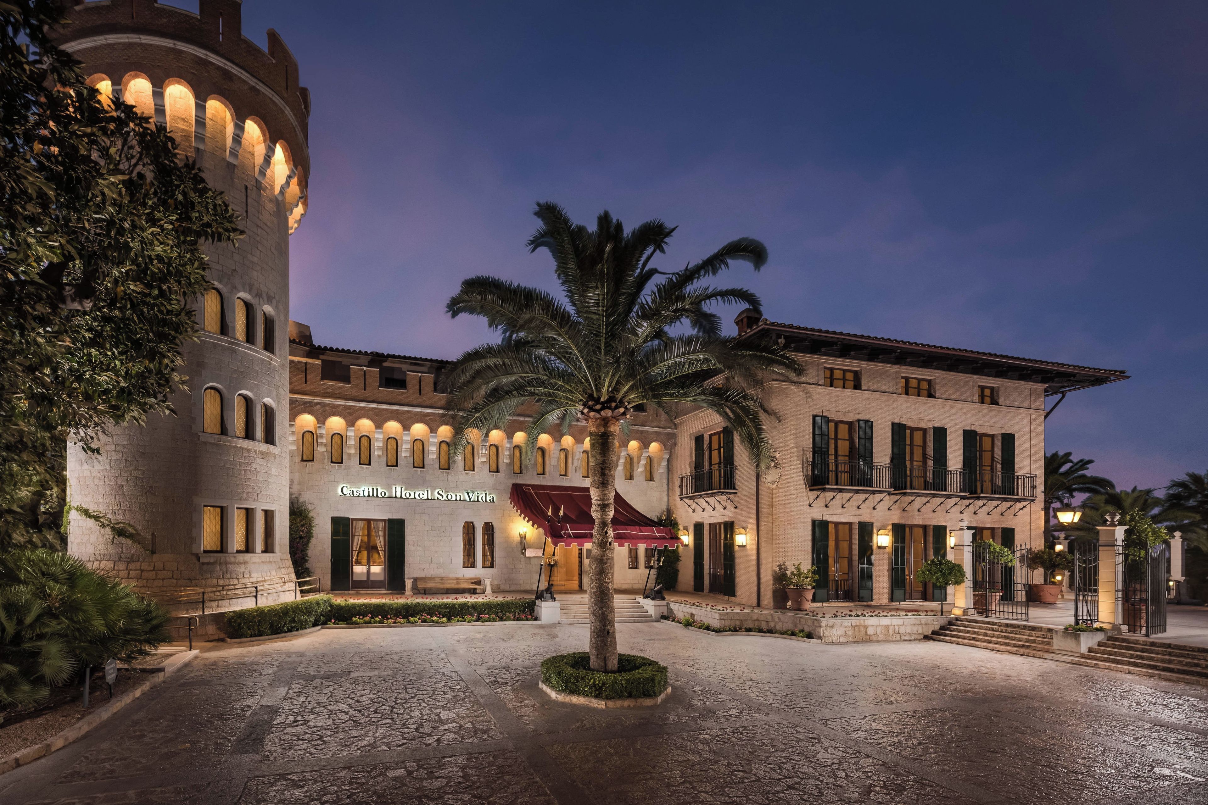 Un edificio histórico con un patio, palmeras y un letrero que dice 'Castillo Hotel Son Vida'.