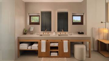 A modern bathroom with a large vanity, two sinks, and a mirror. There are towels and a plant on the vanity, and a small stool in front.