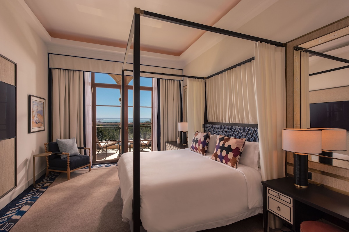 Un lit à baldaquin donnant sur l’extérieur, une chaise, un bureau avec une lampe et un grand miroir.