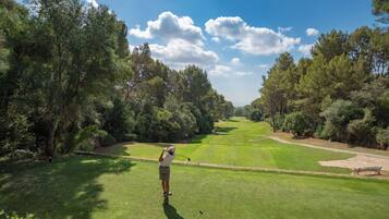 A golf course with a clear sky, lush greenery, and a golfer in mid-swing.