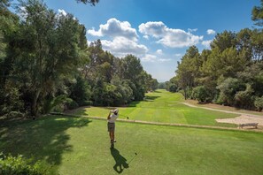 Un terrain de golf sous un ciel dégagé, avec une végétation luxuriante, et un golfeur en plein élan.