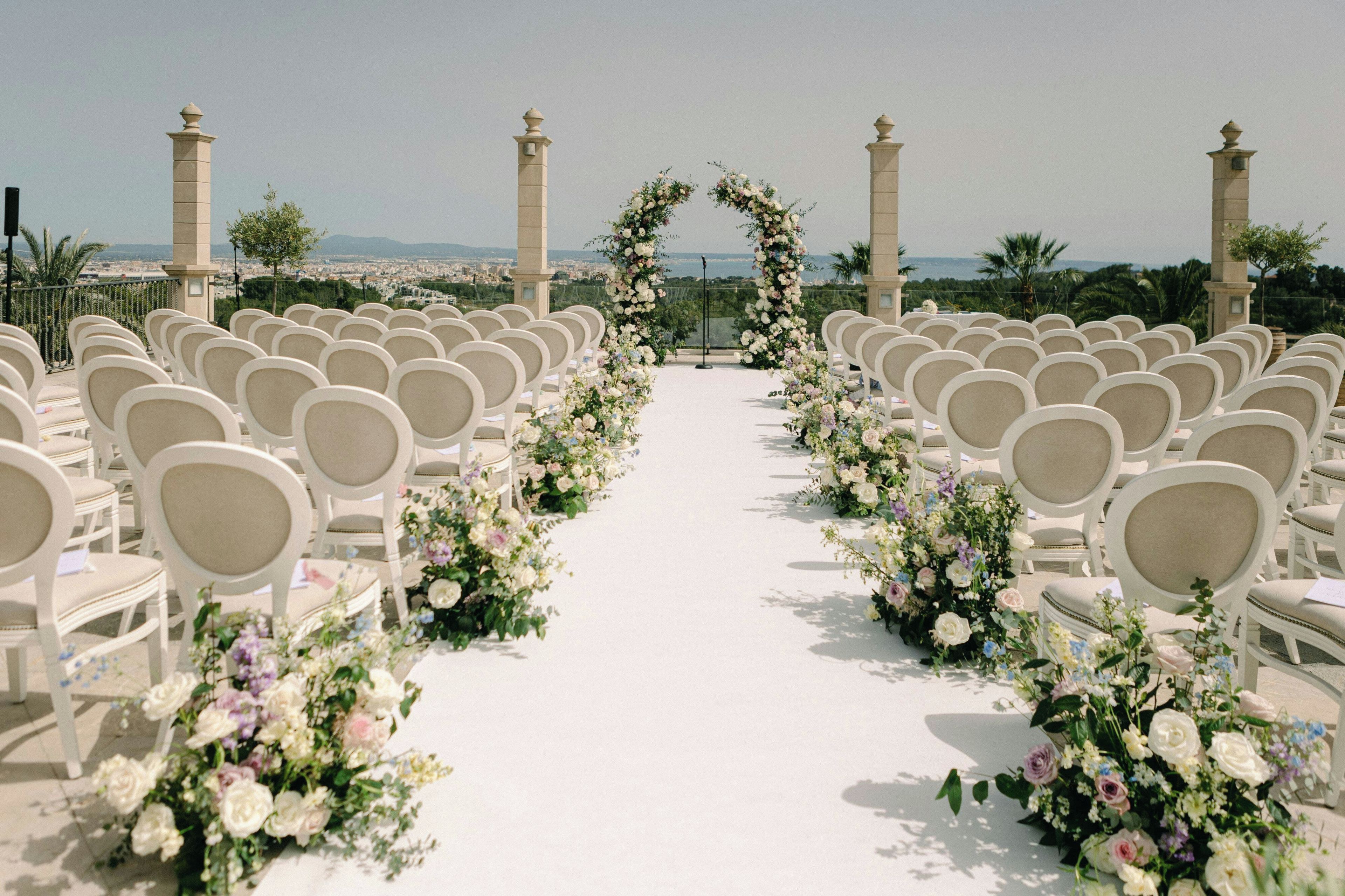 Un pasillo nupcial con sillas blancas y decoración floral.