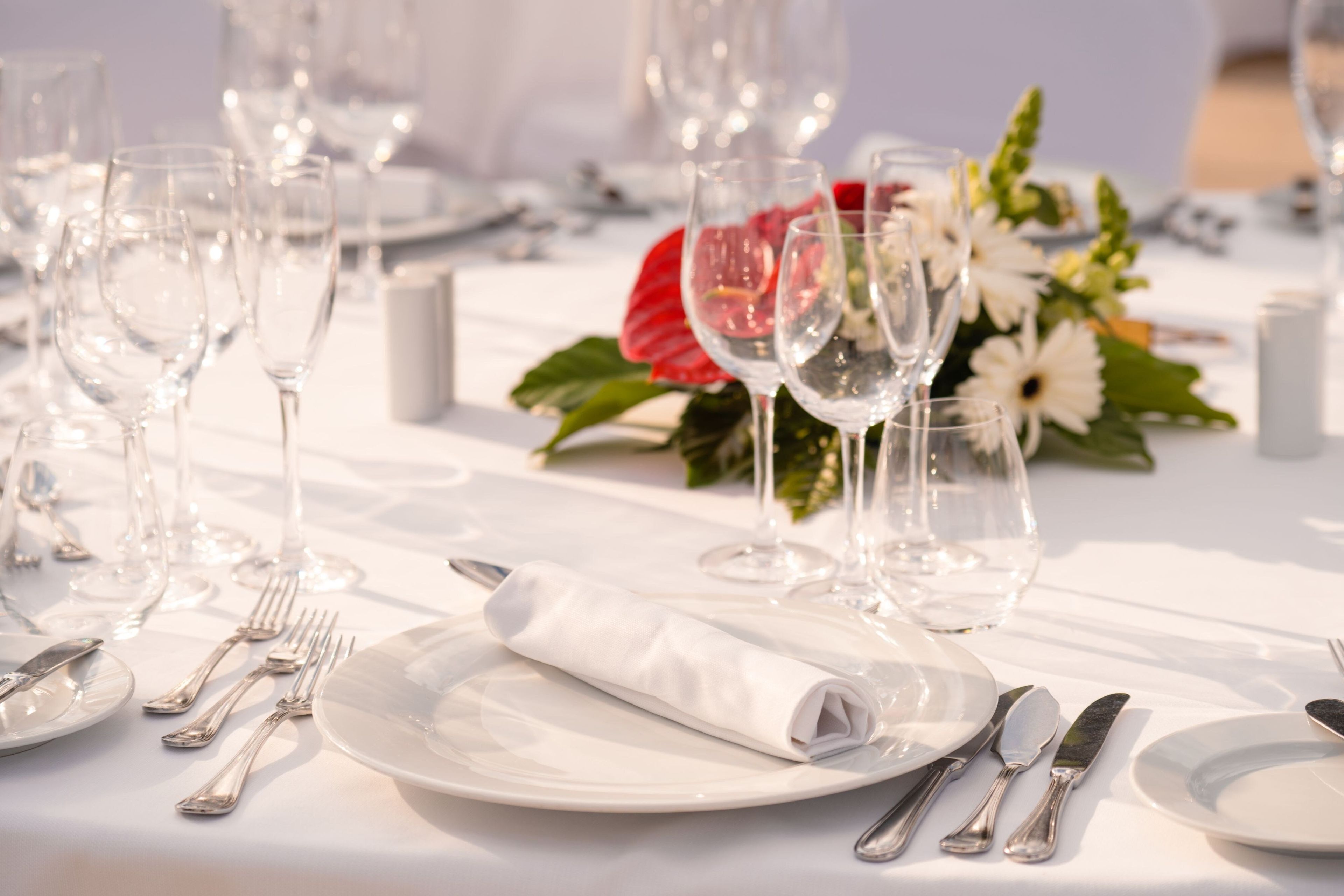 Una mesa dispuesta para un evento de cena formal, con copas de cristal, cubiertos y una servilleta blanca doblada.