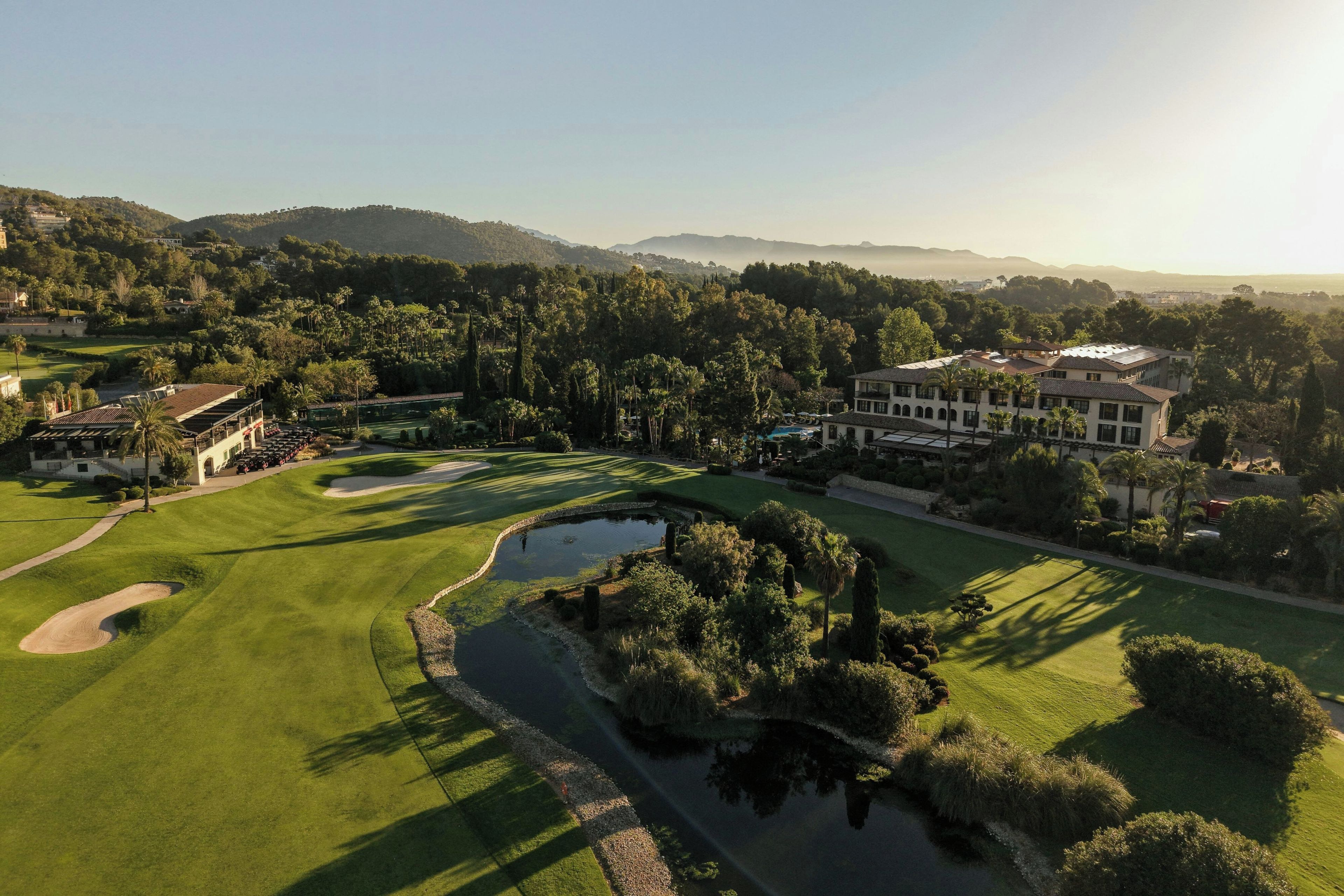 Un campo de golf con un estanque, rodeado de árboles y un edificio grande.